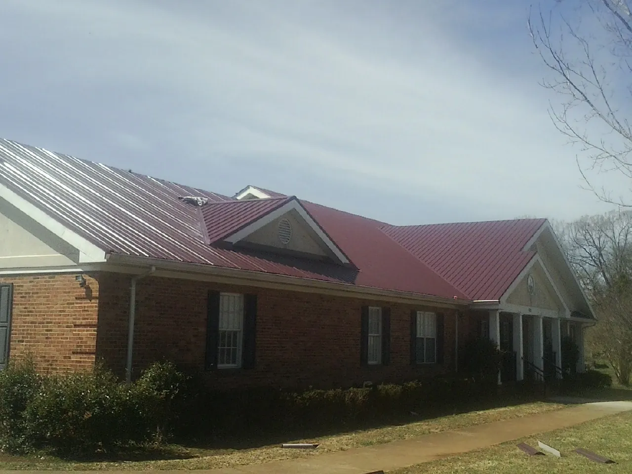 Red metal roof with gabled entries on a long brick building, from a Hail Damage Roof Repair job in Summit Argo