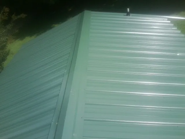 New green metal panels meeting at the ridge of a roof — Flat Roof Repair work by our crew in Summit Argo