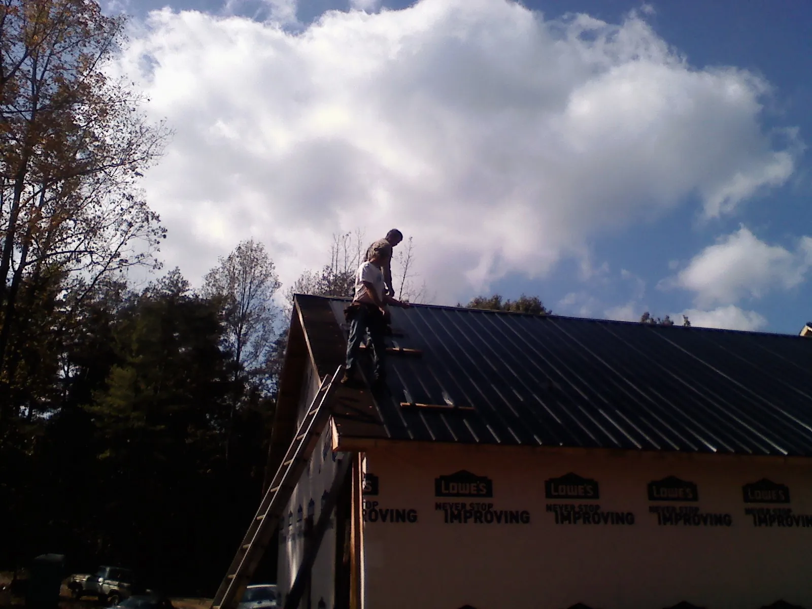 Roofer fastening dark metal panels high against a cloudy sky, from a Roof Inspection job in Summit Argo